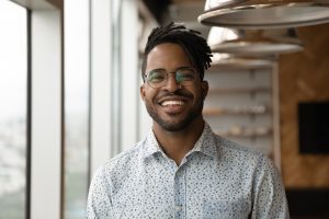 Profile picture of smiling young African American man in glasses pose in own home apartment. Close up headshot portrait of happy millennial biracial male renter or tenant in spectacles show optimism.